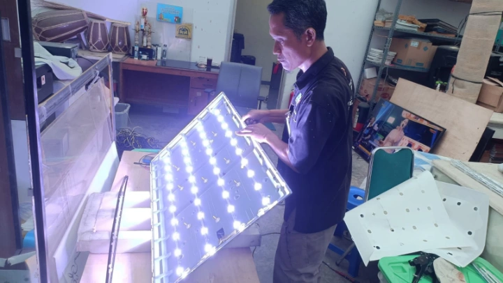Teknisi profesional sedang membongkar TV dan mengetes satu set backlight LED baru pada TV kantor di wilayah Cikarang.